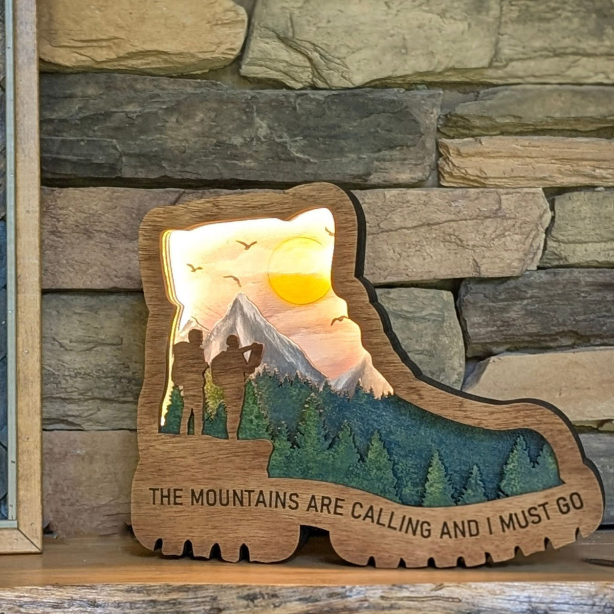 Hiking Boot "The Mountains Are Calling and I Must Go" Featured with the Light On displayed on a mantle
