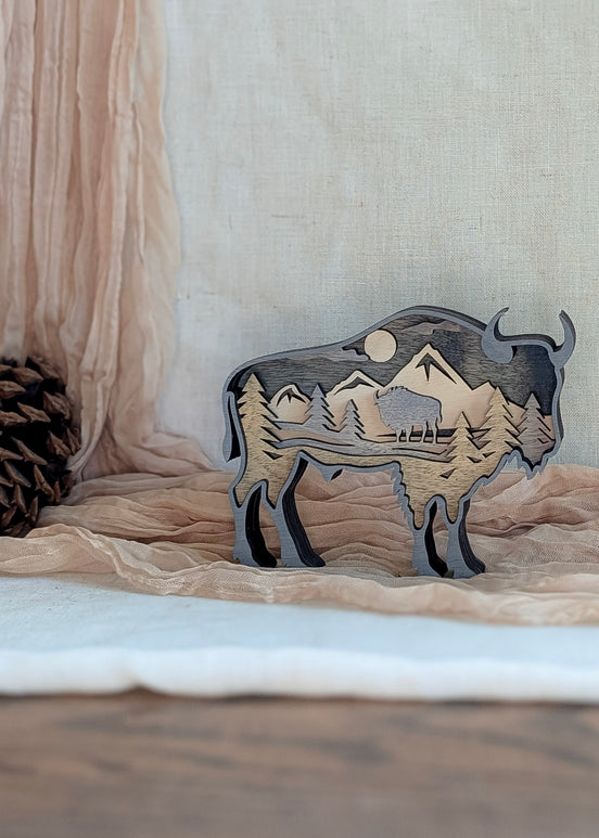 Gray washed layered bison wood art featuring pine trees, moon, and mountain scene in silhouette.