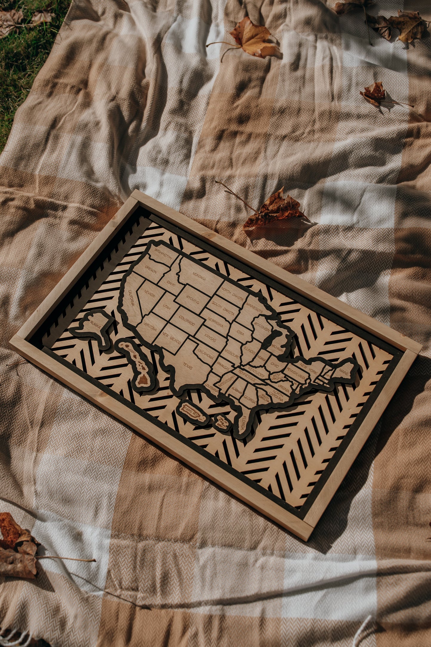 Lifestyle image of the Hearthline Series wooden USA travel map resting on a cozy autumn blanket, symbolizing journeys, memories, and heritage.
