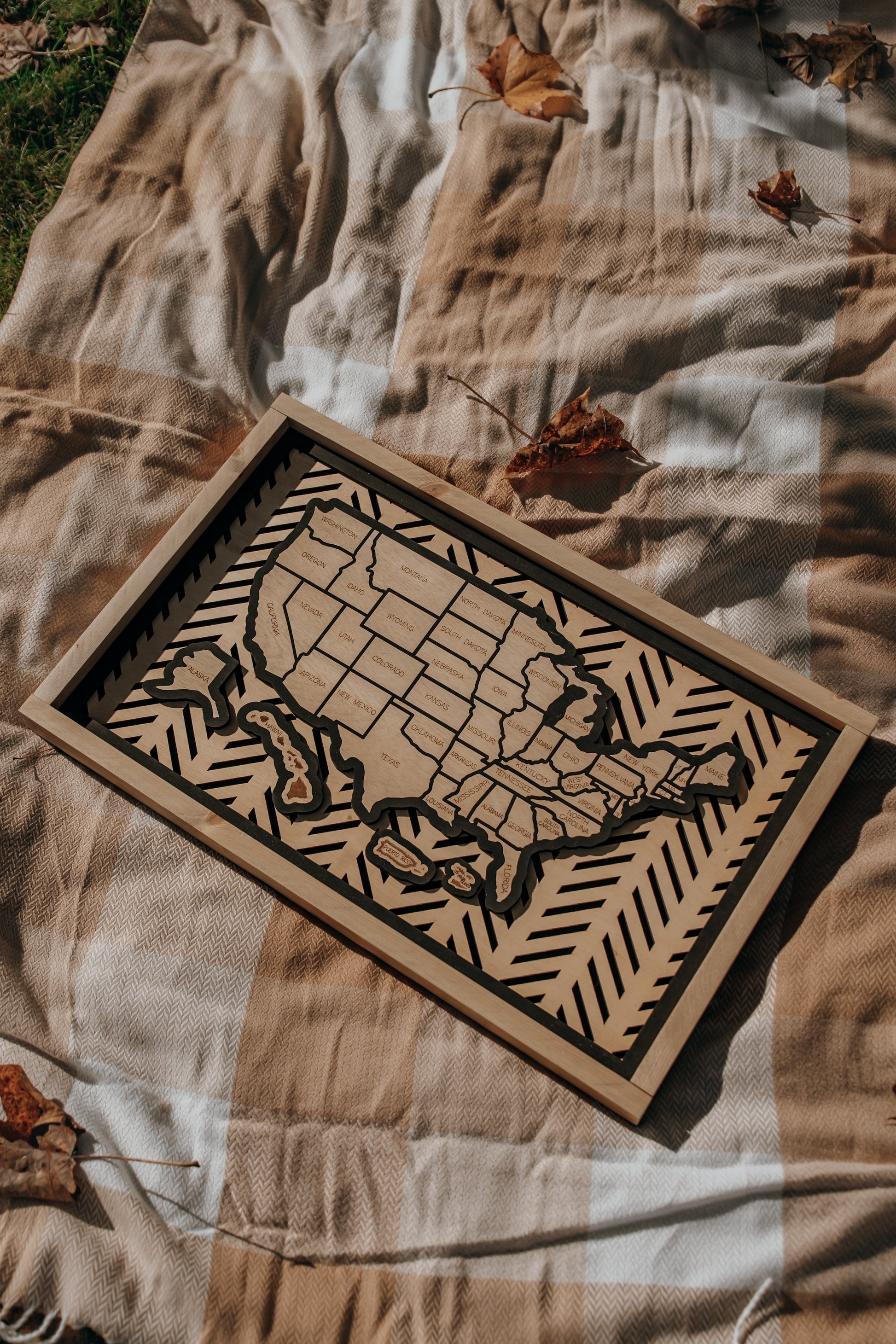 Lifestyle image of the Hearthline Series wooden USA travel map resting on a cozy autumn blanket, symbolizing journeys, memories, and heritage.