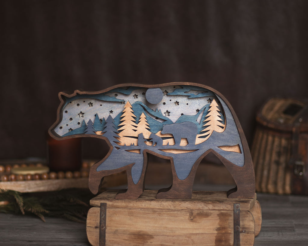 A rustic wooden bear silhouette cutout with layered forest and moon scenery inside, displayed on a wooden stand against a dark brown backdrop.