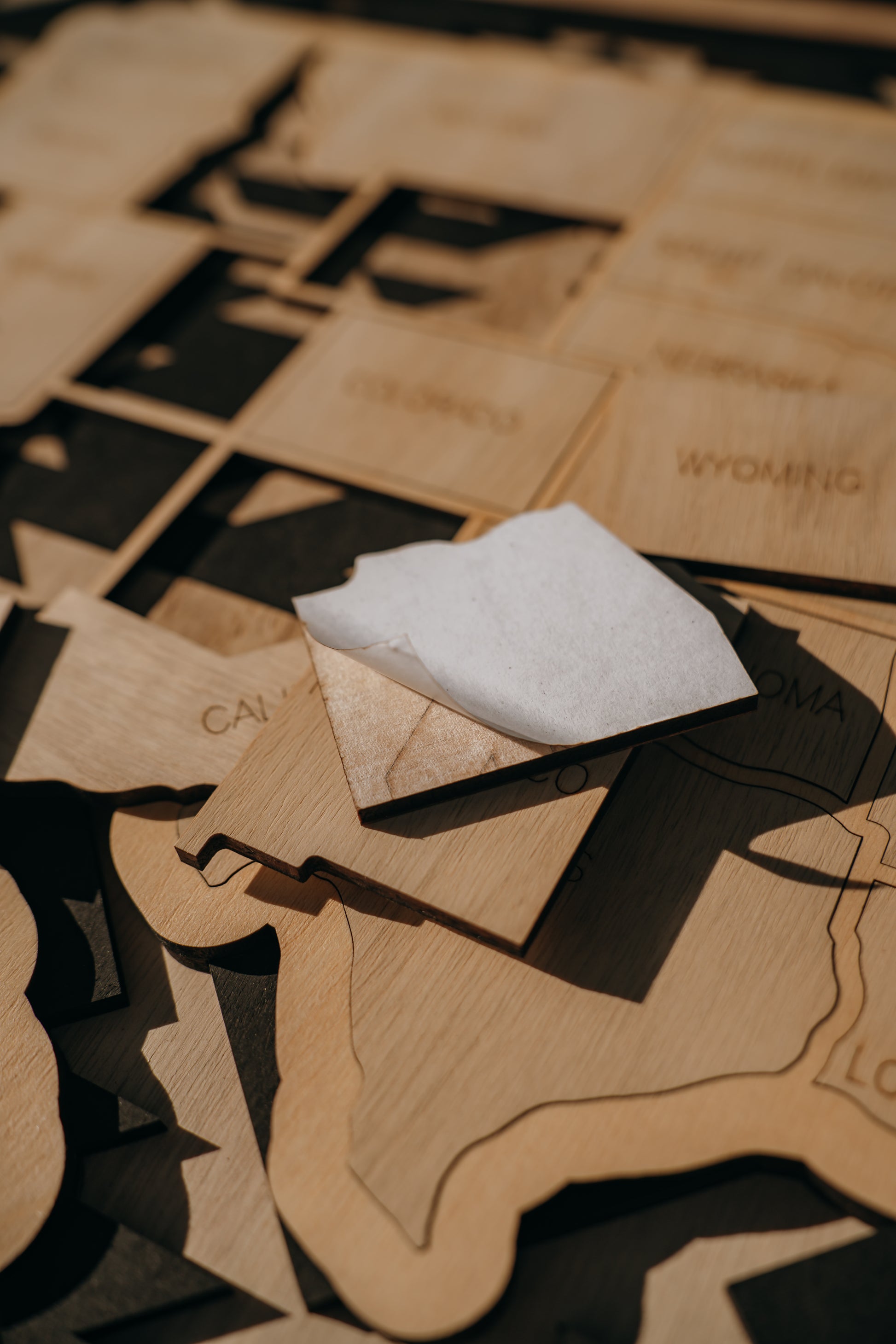Close-up of a wooden state piece with peel-and-stick adhesive backing, part of a handcrafted Storyline Series USA travel map.