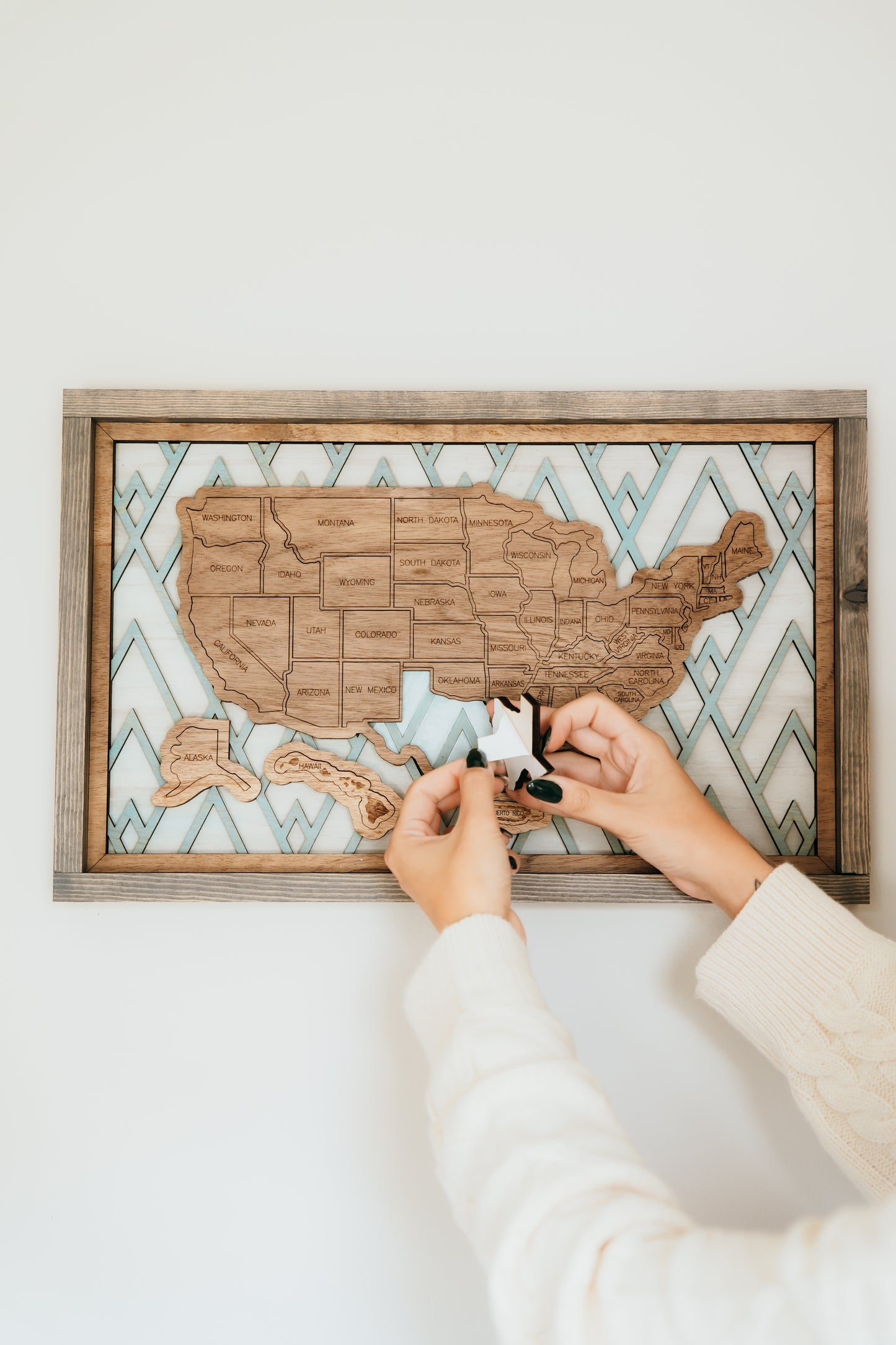 Hands placing wooden state pieces onto the Summit Peaks Storyline Series travel map mounted on a wall.