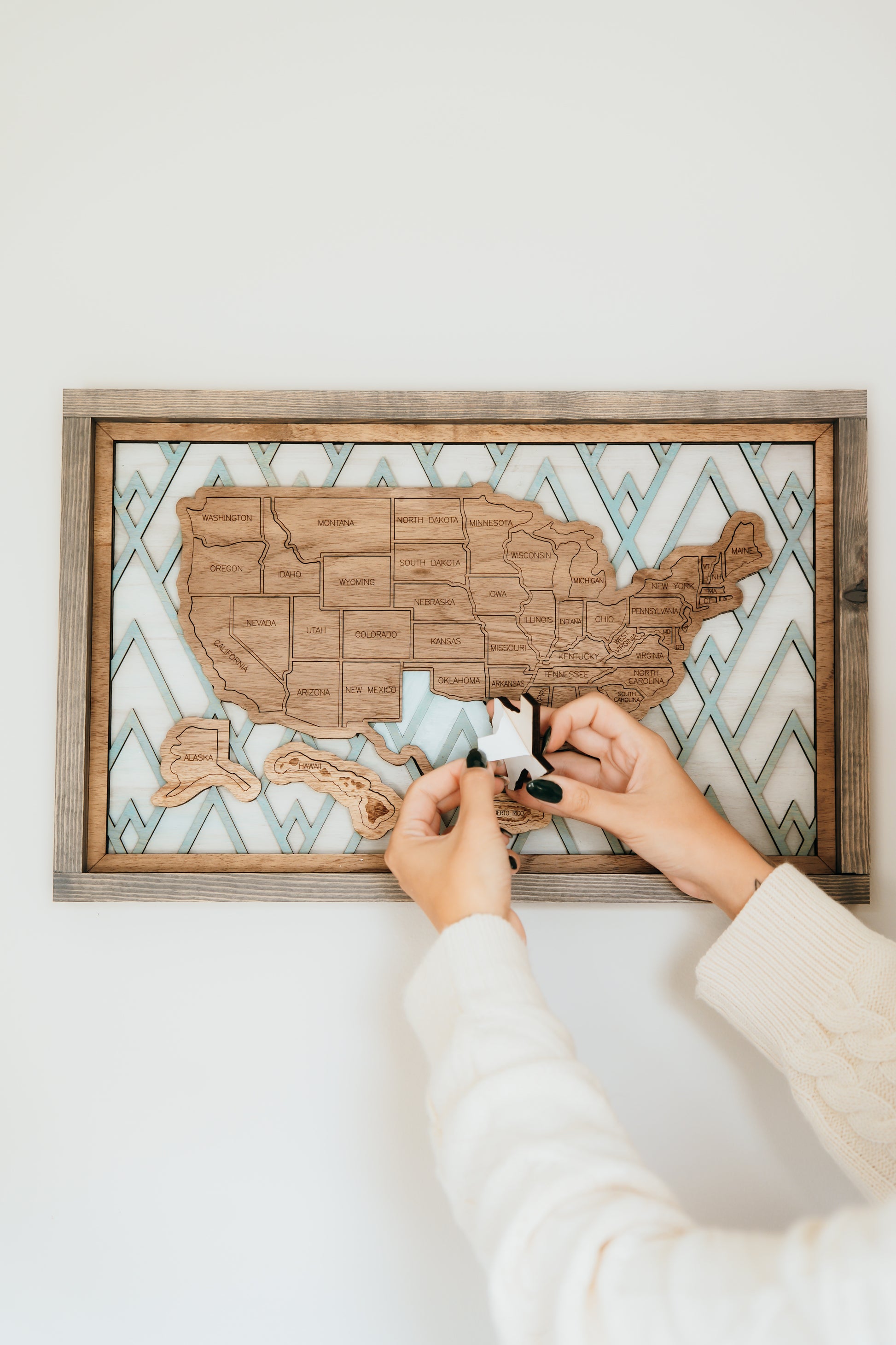 Hands placing wooden state pieces onto the Summit Peaks Storyline Series travel map mounted on a wall.
