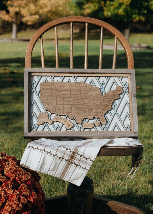 Summit Peaks handcrafted wooden travel map displayed as wall art, styled on a vintage chair with fall decor. 