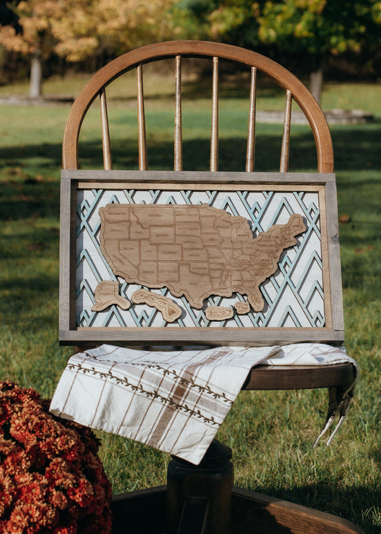 Summit Peaks handcrafted wooden travel map displayed as wall art, styled on a vintage chair with fall decor. 