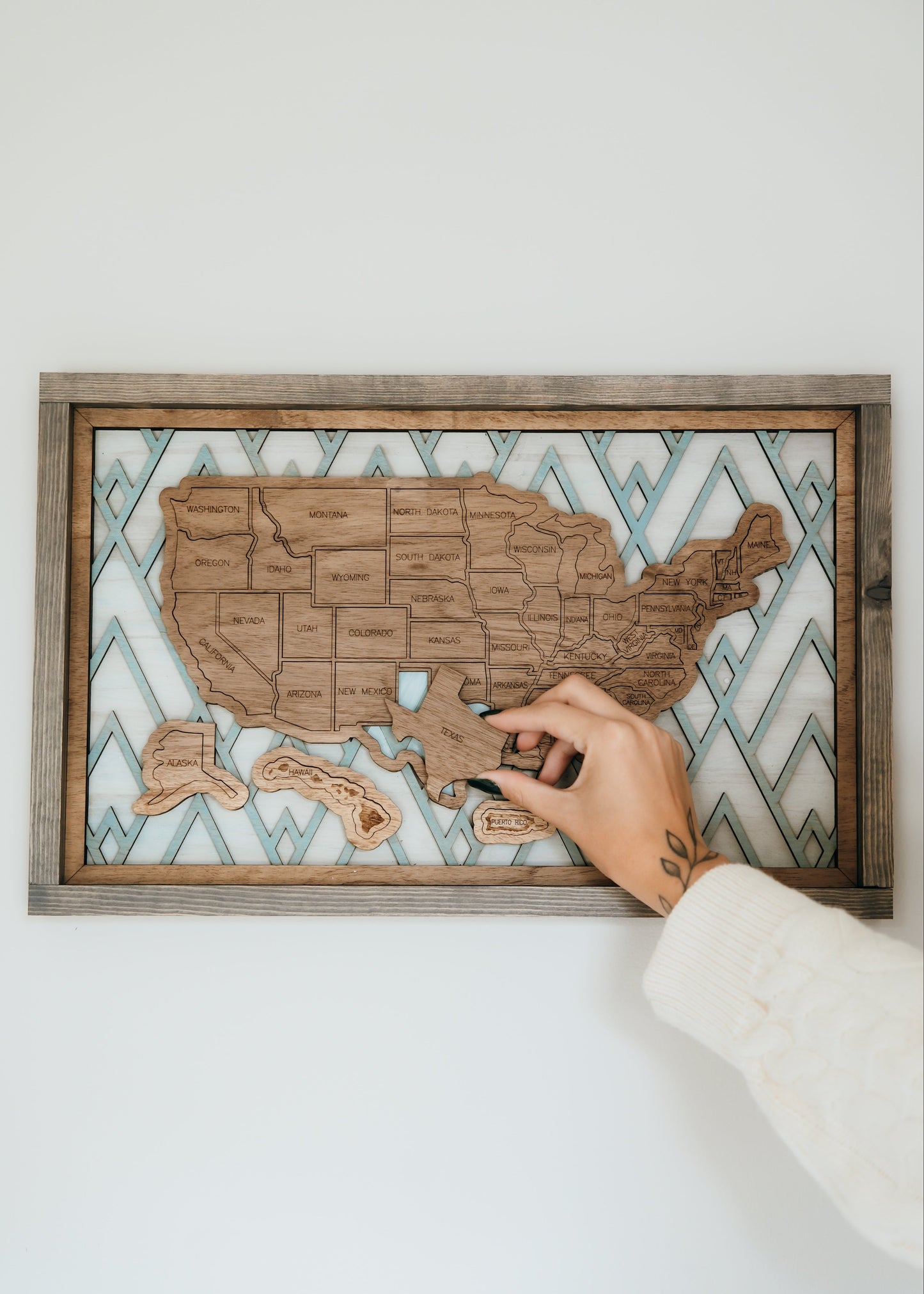 Hand placing a wooden state piece onto the Summit Peaks travel map from the Storyline Series, featuring a mountain-inspired background.