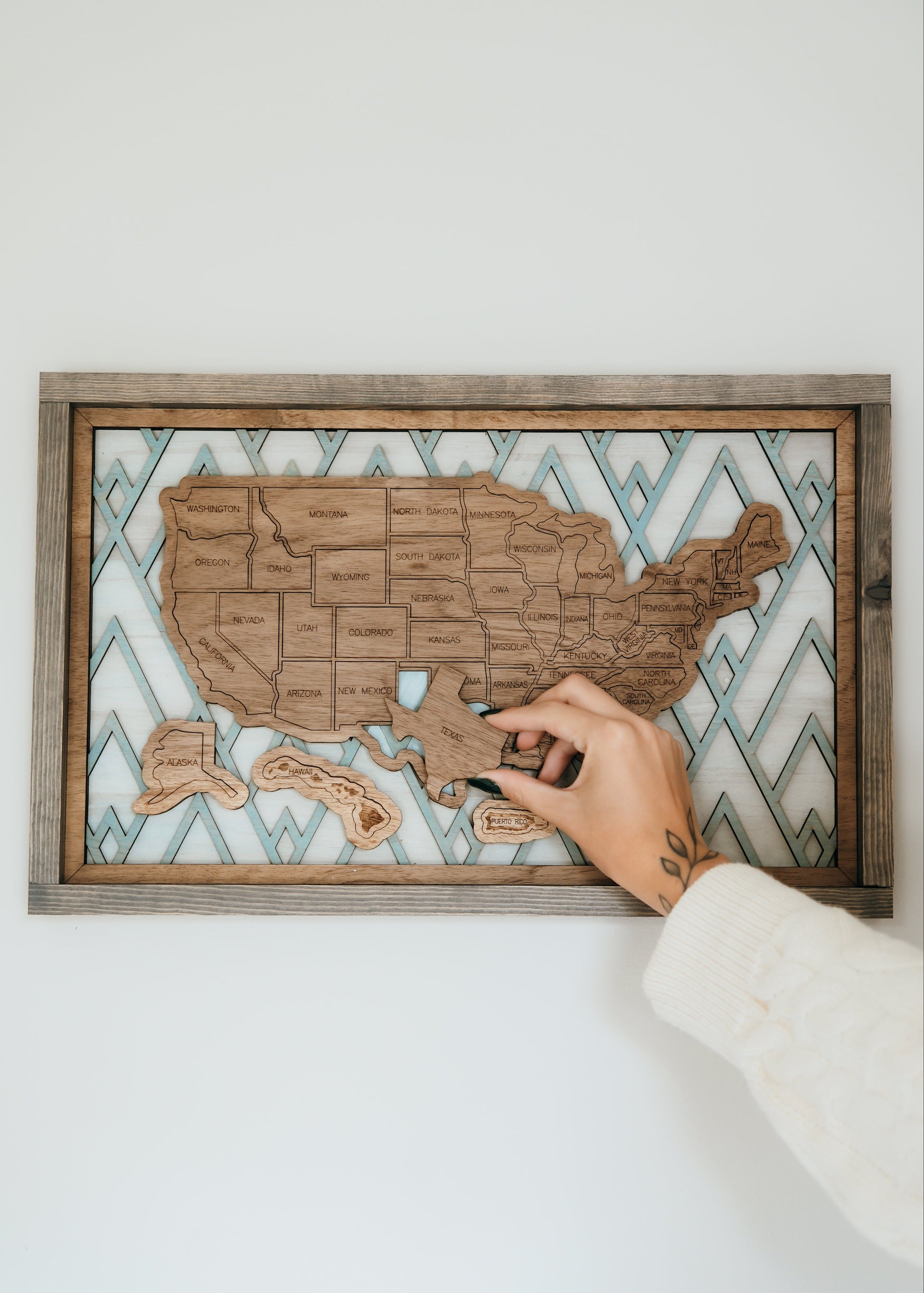 Hand placing a wooden state piece onto the Summit Peaks travel map from the Storyline Series, featuring a mountain-inspired background.