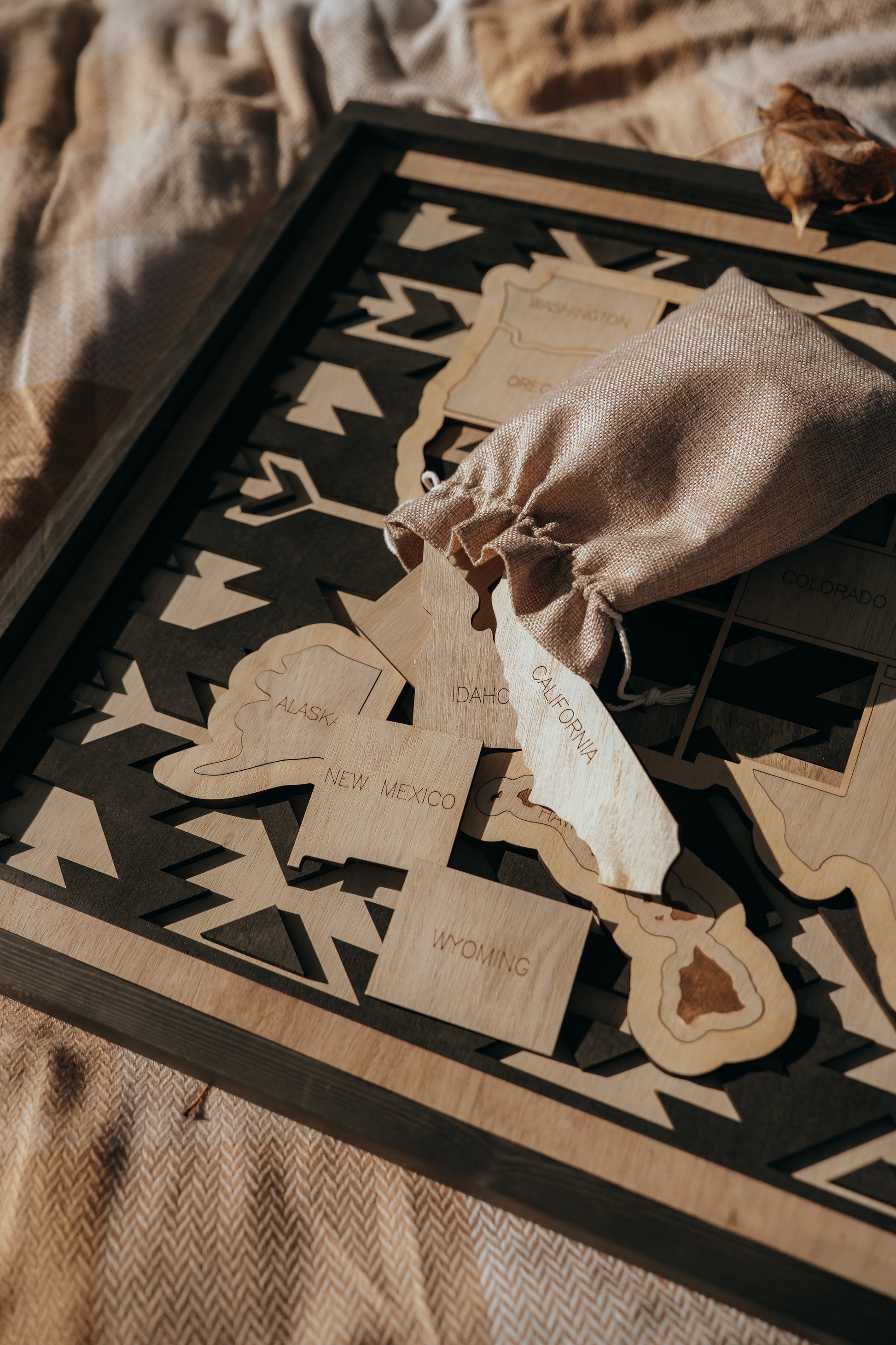 Engraved wooden state pieces spilling from a burlap storage bag onto the Storyline Series USA travel map.