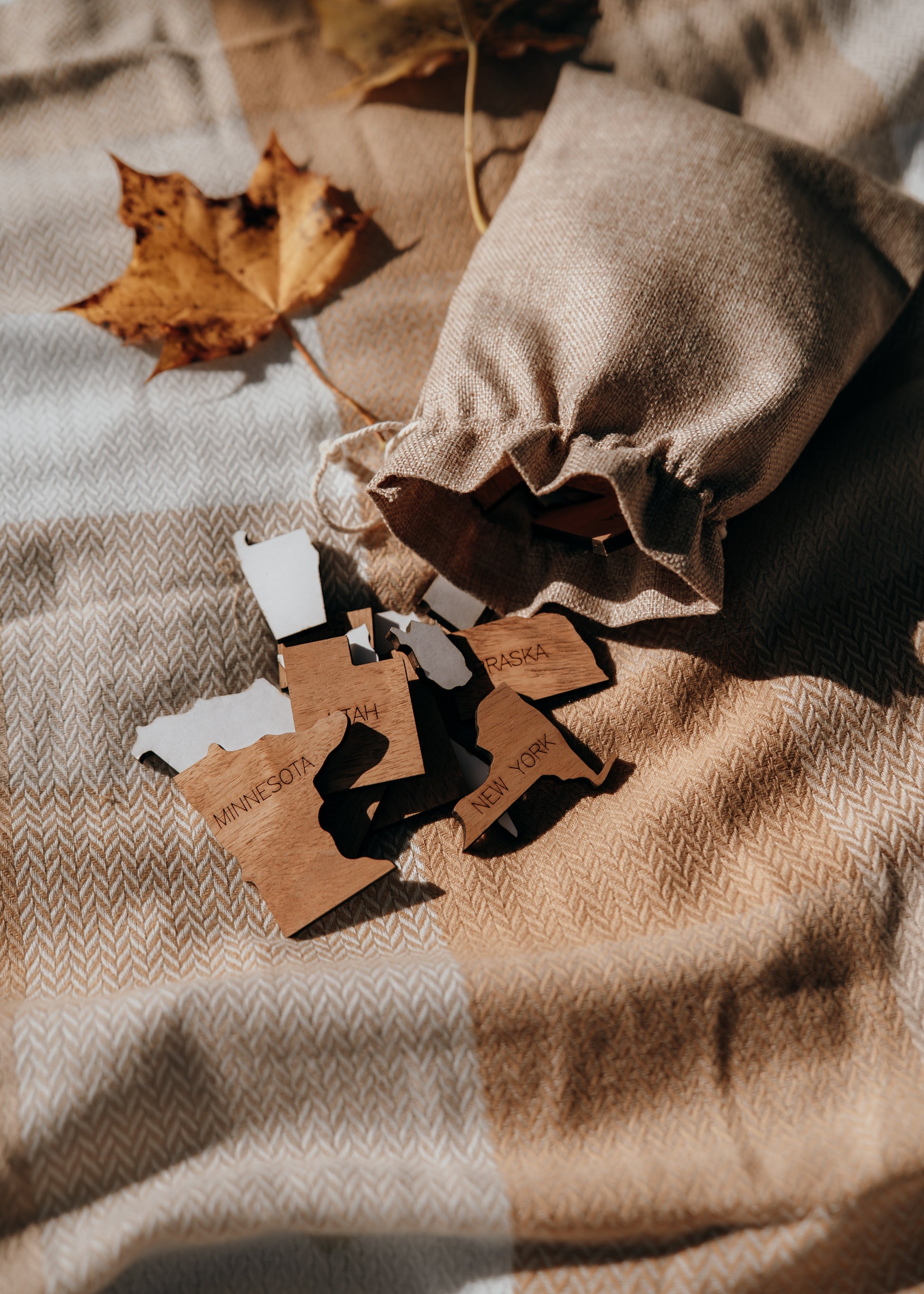 Wooden state pieces with peel-and-stick backing shown with burlap storage bag for the Storyline Series handcrafted travel map.